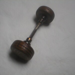 May include: A vintage wooden door knob with a dark brown finish. The knob has a cylindrical shape with a series of horizontal grooves. The connecting rod is a dark metal. The knob is likely from an antique door.