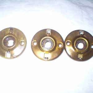 May include: Three gold-colored metal door knobs with a round shape and a hole in the center. The knobs have a slightly worn finish.