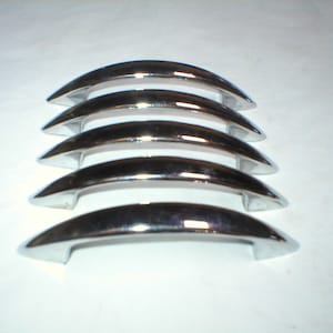 May include: Five chrome cabinet door pulls in a staggered stack. The pulls are curved and have a smooth, shiny finish.