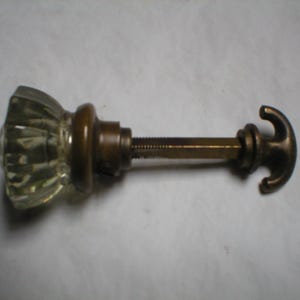 May include: A clear glass door knob with a brass backplate and a hook-shaped metal spindle.