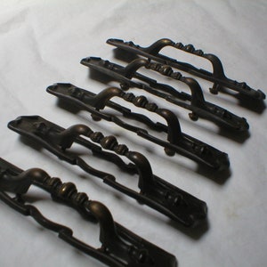 May include: Six antique brass cabinet door pulls with ornate designs. The pulls are in various sizes and have a slightly aged finish.