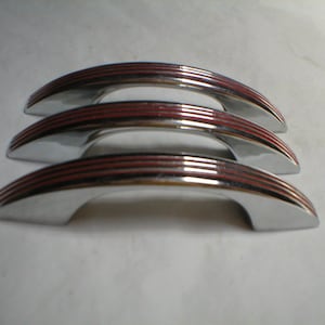 May include: Three chrome cabinet door pulls with red accent stripes. The pulls are curved and have a smooth, polished finish.