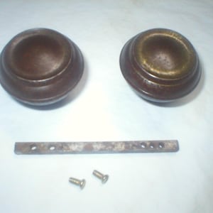 May include: Two antique bronze cabinet knobs with a decorative design. The knobs are round with a slightly domed top and a circular base. Also included are a metal bar with holes and two screws.