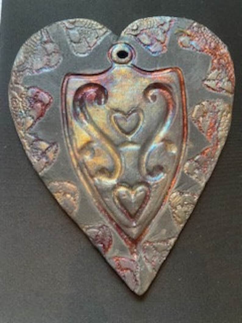 A heart embossed shape pressed into a Raku clay piece, bisque fired, then raku glazed fired outside in raku kiln. copper, gold colors image 1