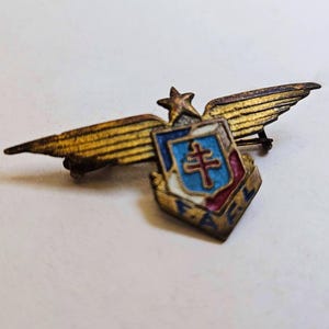 Peut inclure: Ancien insigne militaire en laiton avec un écusson, une croix et les lettres "FA". L'insigne a des ailes et une étoile, avec des détails en émail bleu, rouge et blanc. Un objet de collection.