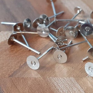 May include: A pile of silver earring posts with flat round backs. The posts are approximately 2.5 cm long and the backs are about 1.25 cm in diameter.