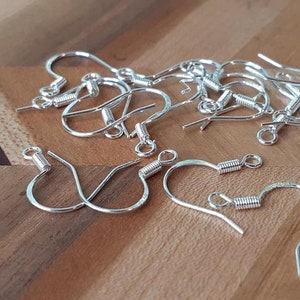 May include: A close-up of a group of silver earring hooks. The hooks are made of metal and have a spring-loaded closure. They are ideal for making your own earrings.