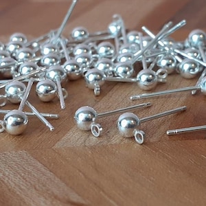 May include: A pile of silver earring posts with small round balls on the ends. The posts are scattered on a wooden surface.