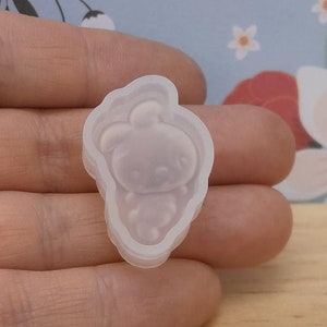 May include: A clear silicone bunny-shaped mould. The mould is held in a hand, with a light blue floral patterned background. The bunny mould has a detailed face and body.