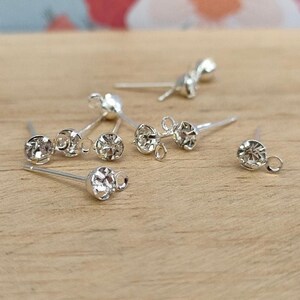 May include: Silver earring findings with clear rhinestones. The findings have a loop at the top and a post with a small bead at the end.