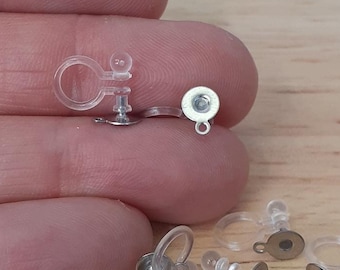 May include: A close-up of a set of clear plastic earring backs with silver metal posts and backs. The earring backs are designed to be used with clip-on earrings.