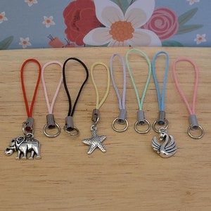 May include: Seven colourful string phone charms with different silver charms attached. The charms include an elephant, a starfish, and a swan.
