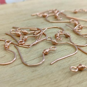 May include: A pile of rose gold earring hooks. The hooks are made of metal and have a small loop at the top. They are perfect for making earrings.