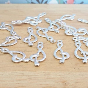 Puede incluir: Una colección de abalorios de metal plateados en forma de claves de sol. Los abalorios están esparcidos sobre una superficie de madera.