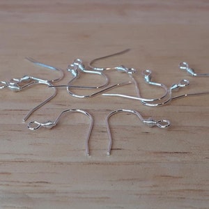 May include: A group of silver earring hooks with a twisted wire detail. The hooks are scattered on a wooden surface.