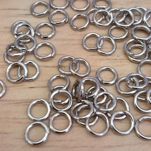 May include: A large pile of silver jump rings. The rings are small and round, and they are all the same size.