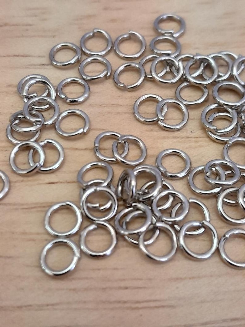 May include: A large pile of silver jump rings. The rings are small and round, and they are all the same size.