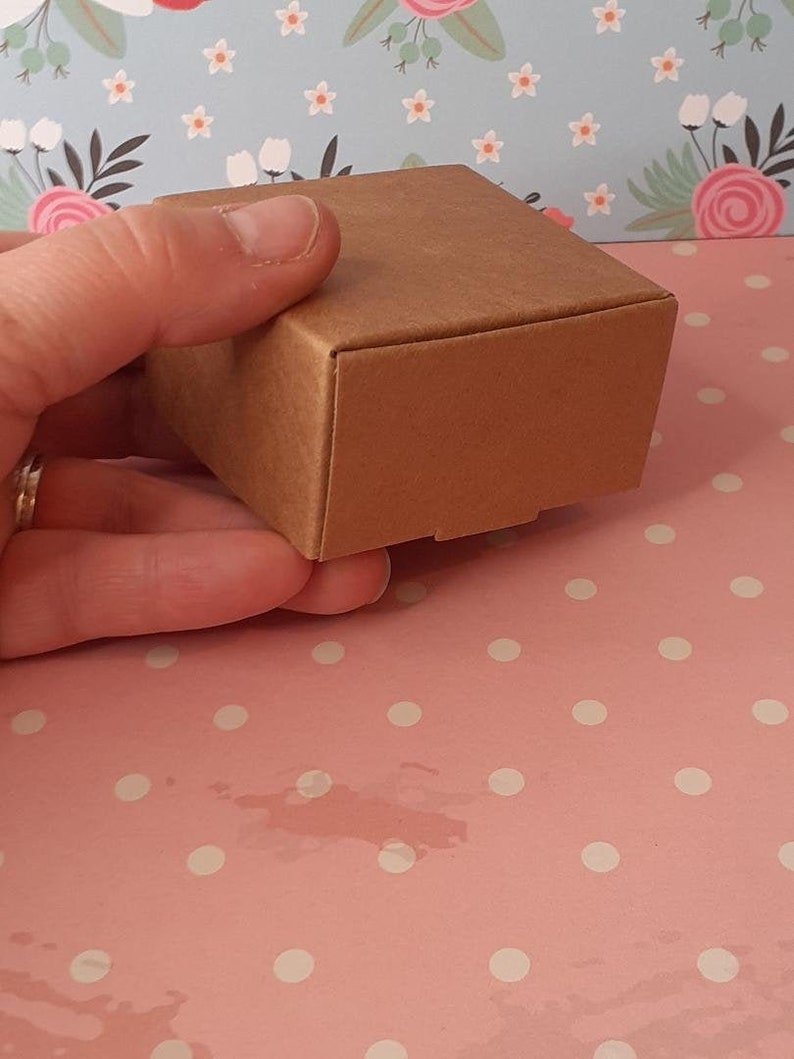 K&ouml;nnte beinhalten: Eine kleine, quadratische Schachtel aus braunem Karton. Die Schachtel ist aus robustem Karton und hat eine glatte, matte Oberfl&auml;che.