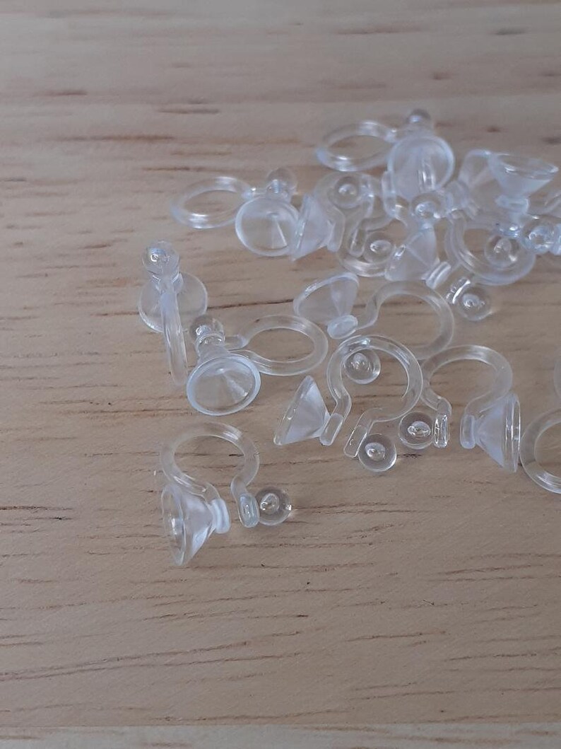May include: A group of clear plastic earring backs with a small loop and a suction cup on the back.