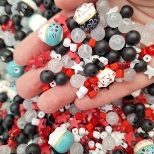 May include: A mix of red, white, black and blue beads, including star-shaped beads, square beads, round beads, and small ceramic beads with a Japanese design.