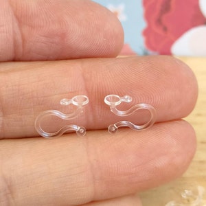 May include: Two clear plastic curtain clips, designed to hold curtains in place. The clips are shaped like a hook with a small loop at the end.