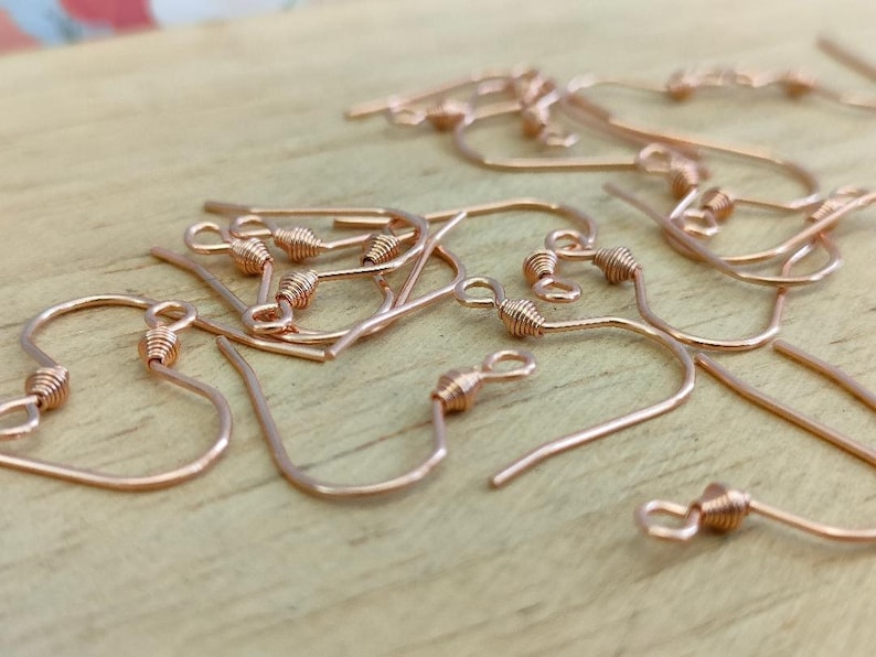 May include: A pile of rose gold earring hooks. The hooks are made of metal and have a small loop at the top. They are perfect for making earrings.