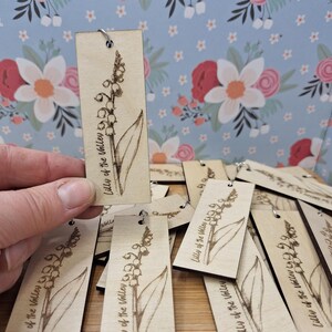 May include: Light brown wooden tags with a Lily of the Valley design. Each tag has a floral illustration and the text "Lilly of the Valley". The tags have a small metal ring at the top for hanging.