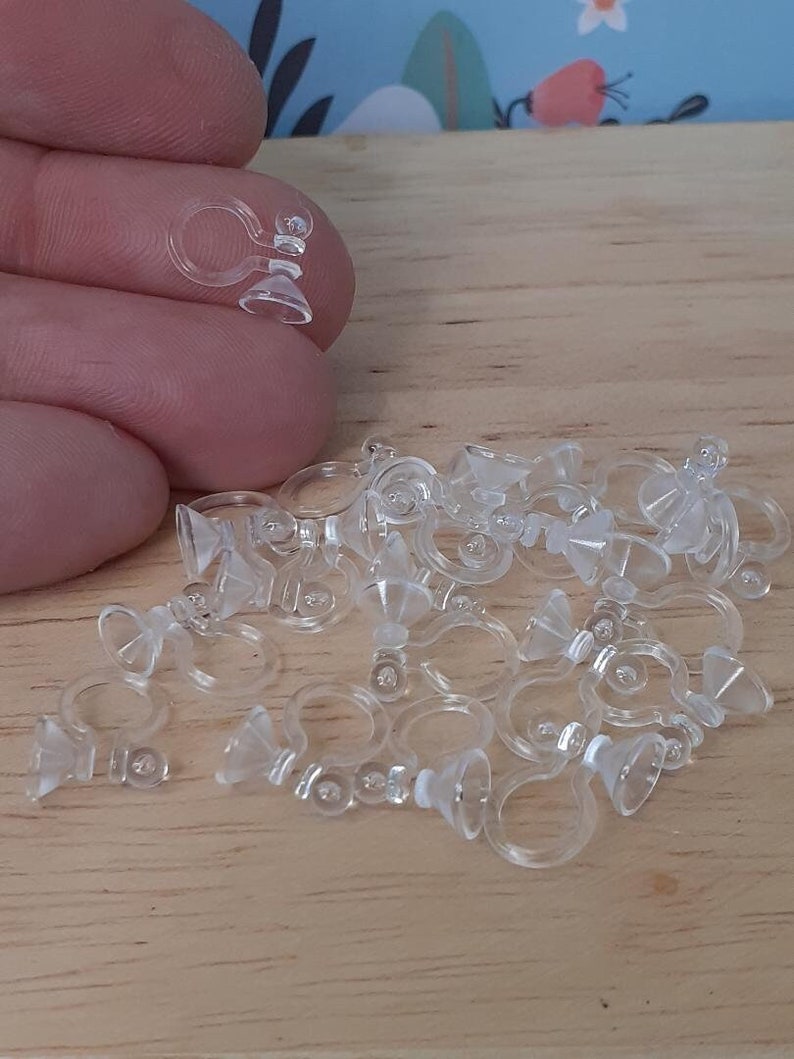 May include: A pile of clear plastic earring backs with a suction cup on the bottom. The earring backs are designed to be used with clip-on earrings.