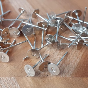 May include: A pile of silver earring posts with flat round backs. The posts are approximately 2.5 cm long and the backs are about 1.25 cm in diameter.