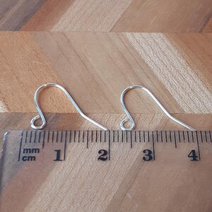 May include: Two silver earring hooks measuring 3 cm in length, placed on a wooden surface next to a ruler.