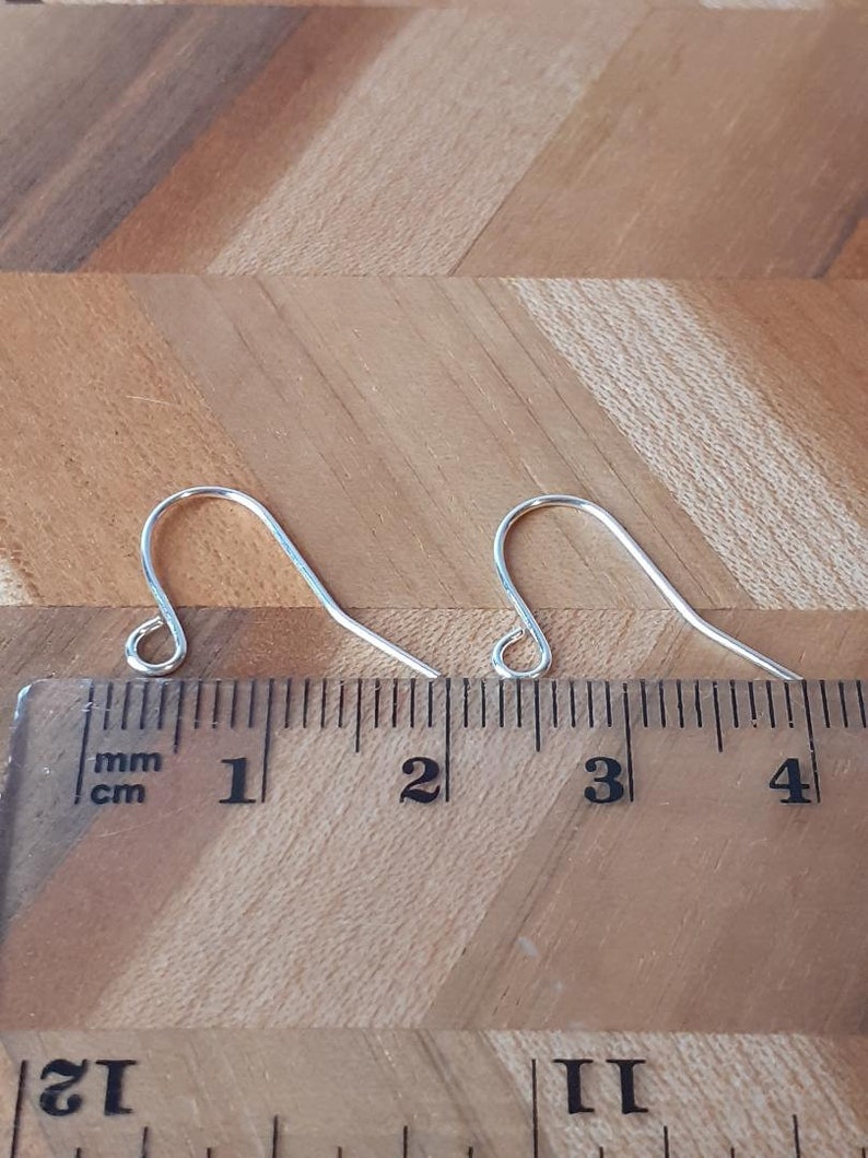 May include: Two silver earring hooks measuring 3 cm in length, placed on a wooden surface next to a ruler.