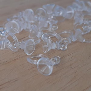 May include: A group of clear plastic suction cup hooks with a ring on the top. The hooks are scattered on a light wood surface.