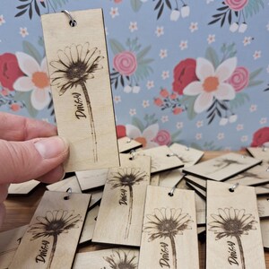 May include: Wooden daisy keyrings with a floral design. Each keyring features a laser-etched daisy flower and the word "Daisy" in a script font. The keyrings have a small metal ring at the top for attaching keys.