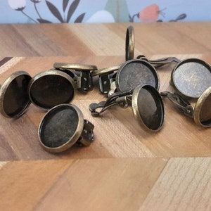 May include: A group of 10 antique gold-toned metal earring settings with round glass cabochons. The settings have a clip-on closure.