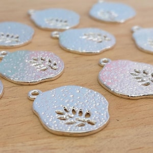 Puede incluir: Encantos de metal plateado con una superficie texturizada y un diseño de hoja. Los encantos están en varios tonos de plata y tienen un acabado ligeramente iridiscente.