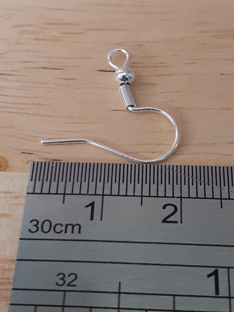 Puede incluir: Gancho para pendientes de plata con una peque&ntilde;a bola en la parte superior, que mide aproximadamente 2,5 cm de largo. El gancho se muestra junto a una regla.