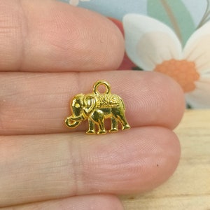 May include: Gold-coloured metal elephant charm with a detailed design. The charm has a loop at the top for attaching to jewellery or other crafts.