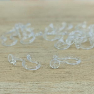 May include: A close-up of a pile of clear plastic hooks. The hooks are designed to hold items like curtains or shower liners.