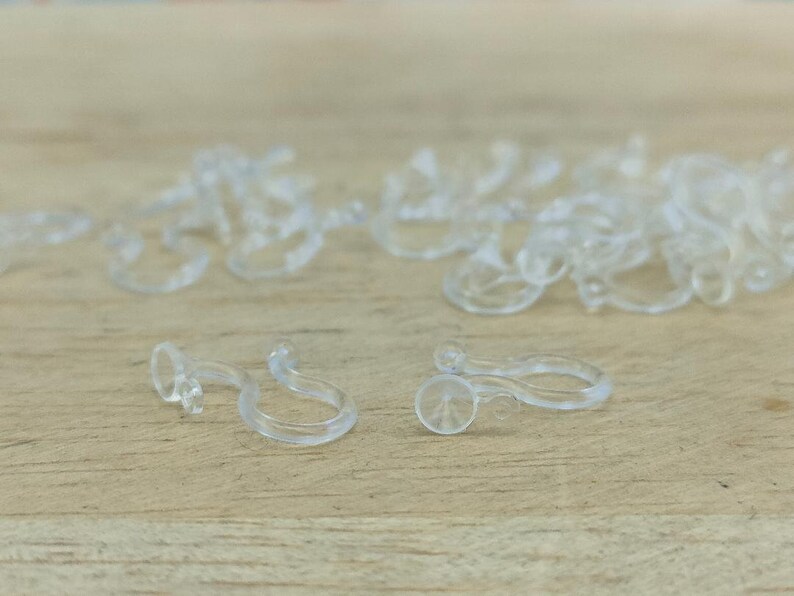May include: A close-up of a pile of clear plastic hooks. The hooks are designed to hold items like curtains or shower liners.