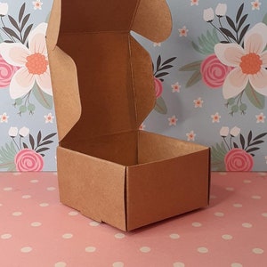 K&ouml;nnte beinhalten: Eine kleine braune Pappbox mit einem Scharnierdeckel. Die Box ist ge&ouml;ffnet und der Deckel ist nach hinten geklappt.
