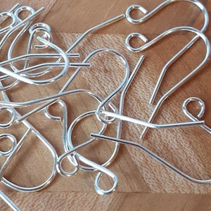 May include: A close-up of a pile of silver earring hooks. The hooks are made of metal and have a smooth finish.