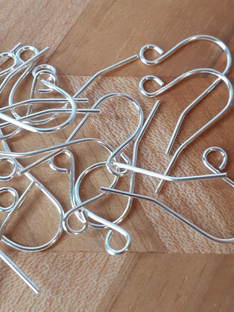 May include: A close-up of a pile of silver earring hooks. The hooks are made of metal and have a smooth finish.
