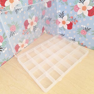 May include: A clear plastic storage box with 16 compartments. The box has a hinged lid and is ideal for organising small items.