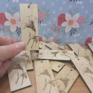 May include: Wooden bookmarks with a floral design. Each bookmark features a detailed engraving of a morning glory flower and the words "Morning Glory". The bookmarks are rectangular with a small hole at the top for a metal ring.