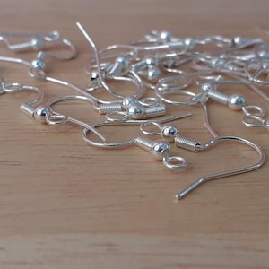 Puede incluir: Primer plano de un mont&oacute;n de ganchos para pendientes de plata. Los ganchos son de metal y tienen una peque&ntilde;a bola en la parte superior. Se utilizan com&uacute;nmente para hacer pendientes.
