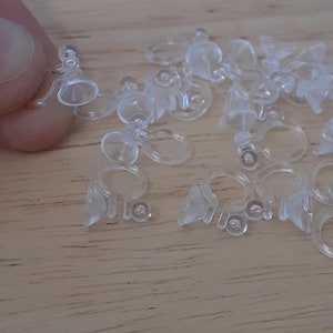 May include: A close-up of a pile of clear plastic earring backs. The backs are designed to be used with post earrings and have a small suction cup on the bottom to help keep them in place.