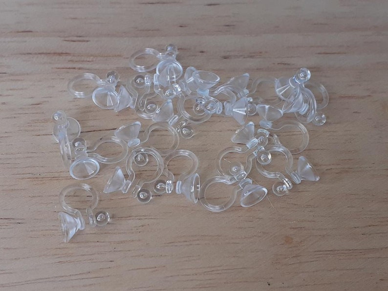 May include: A pile of clear plastic earring backs with a small, clear, cone-shaped piece on the end of each back.