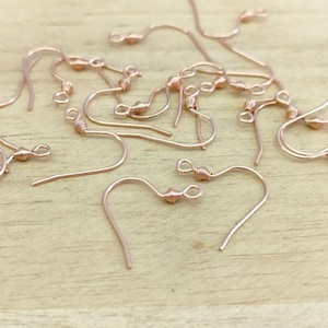 May include: A close-up of a pile of rose gold earring hooks. The hooks are made of wire and have a small loop at the top. The hooks are all twisted at the top to create a decorative effect.