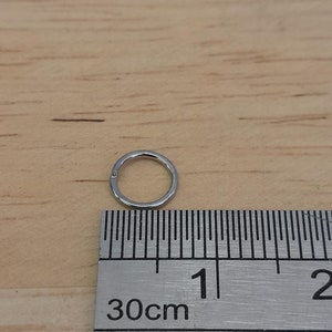 May include: A silver hoop earring measuring 1 cm in diameter, shown next to a ruler.
