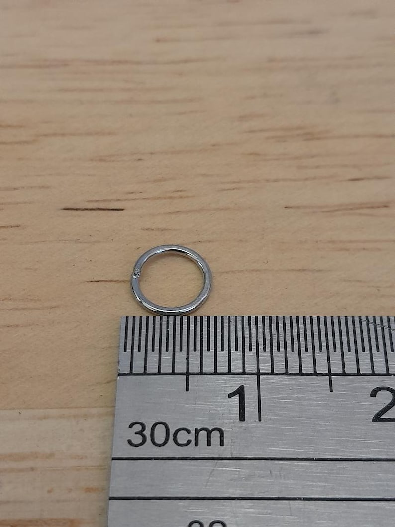 May include: A silver hoop earring measuring 1 cm in diameter, shown next to a ruler.